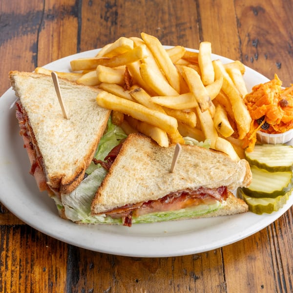 A diner-style club sandwich with fries, coleslaw, and pickles on a white plate.