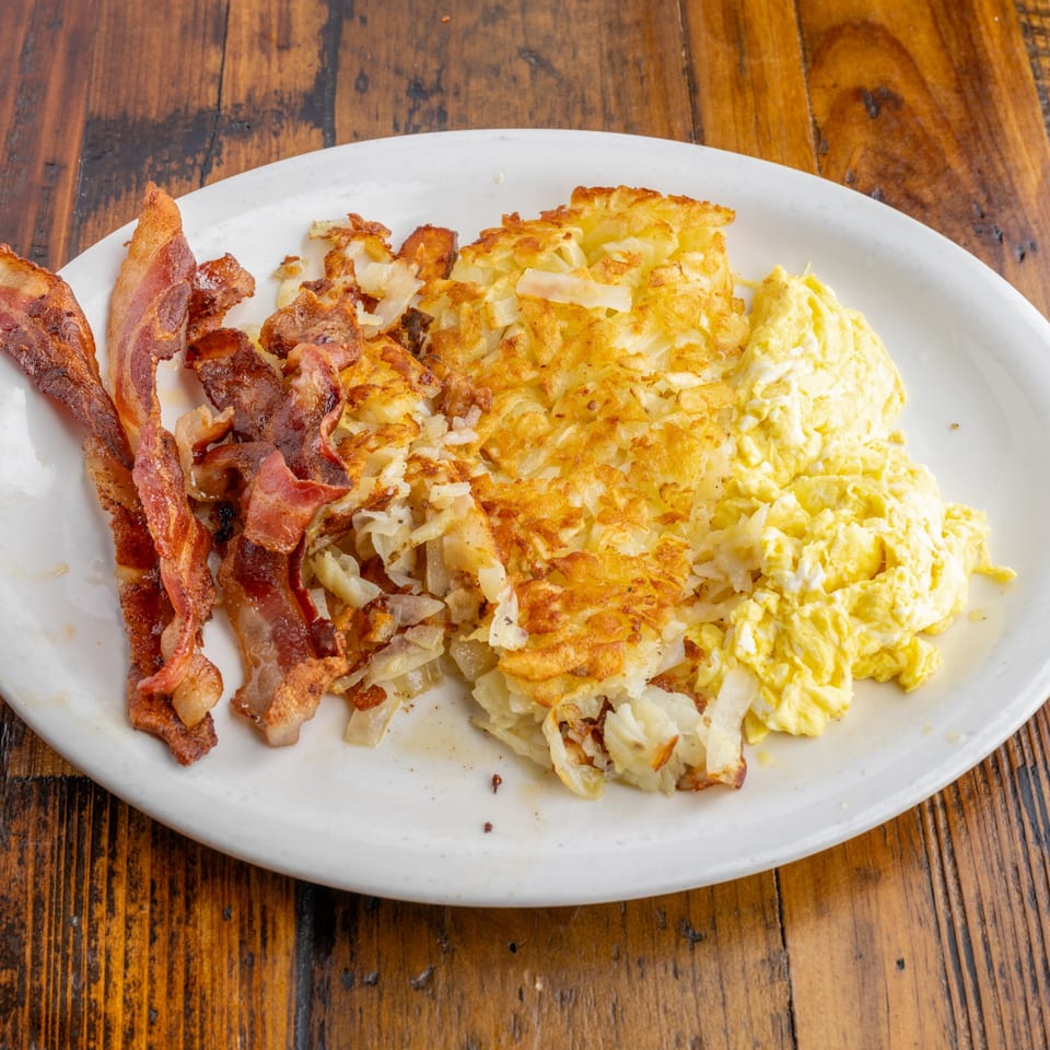A diner breakfast plate with crispy bacon, golden hash browns, and fluffy scrambled eggs.