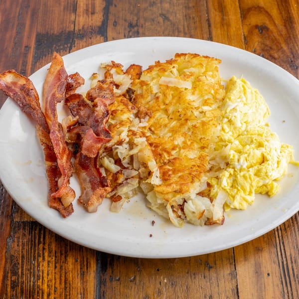 A diner breakfast with crispy bacon, golden hash browns, and fluffy scrambled eggs on a white plate.