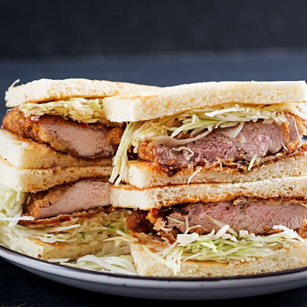 Stacked Crazy Otto's Diner sandwiches with crispy fried pork cutlets and shredded cabbage on white bread.