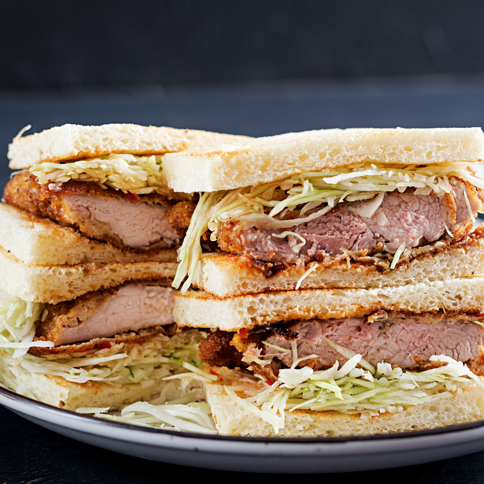 Stacked Crazy Otto's Diner sandwiches with crispy fried pork cutlets and shredded cabbage on white bread.