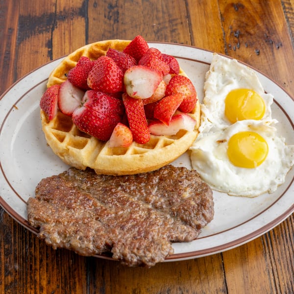 Crazy Otto's Diner breakfast with a waffle topped with strawberries, sausage patty, and two fried eggs.