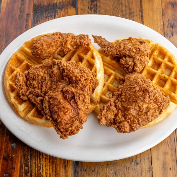 Two golden-brown waffles topped with crispy fried chicken pieces on a white plate.