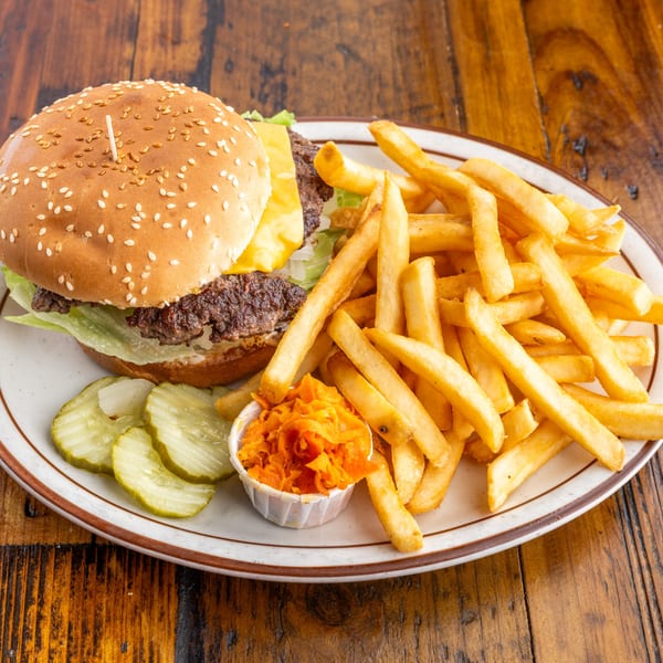 A Crazy Otto's Diner cheeseburger with fries, pickles, and shredded carrots on a white plate.