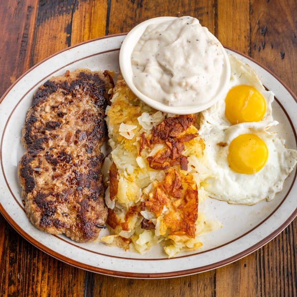 A diner breakfast plate with sausage patties, hash browns, two fried eggs, and a side of gravy.