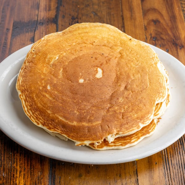 A stack of golden-brown pancakes on a white plate, ready to be served at Crazy Otto's Diner.