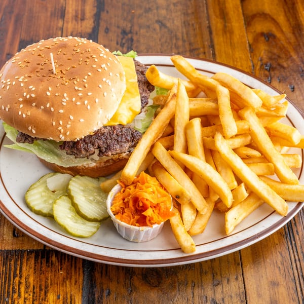 A Crazy Otto's Diner cheeseburger with fries, pickles, and coleslaw on a white plate.