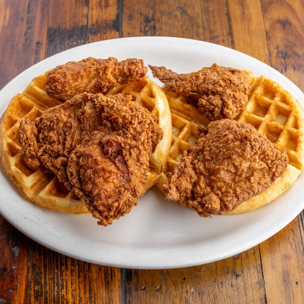 Crispy fried chicken pieces on two golden waffles, served on a white plate at Crazy Otto's Diner.