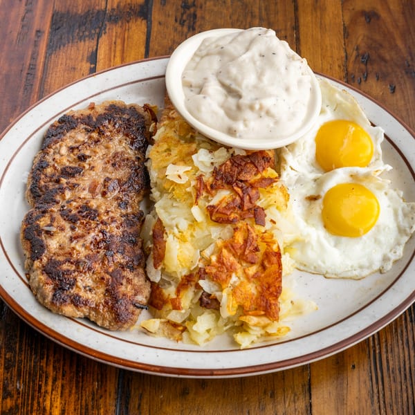 A diner breakfast plate with two sausage patties, hash browns, two fried eggs, and a side of gravy.