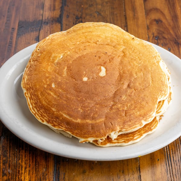 A stack of golden-brown pancakes on a white plate, resting on a rustic wooden table.
